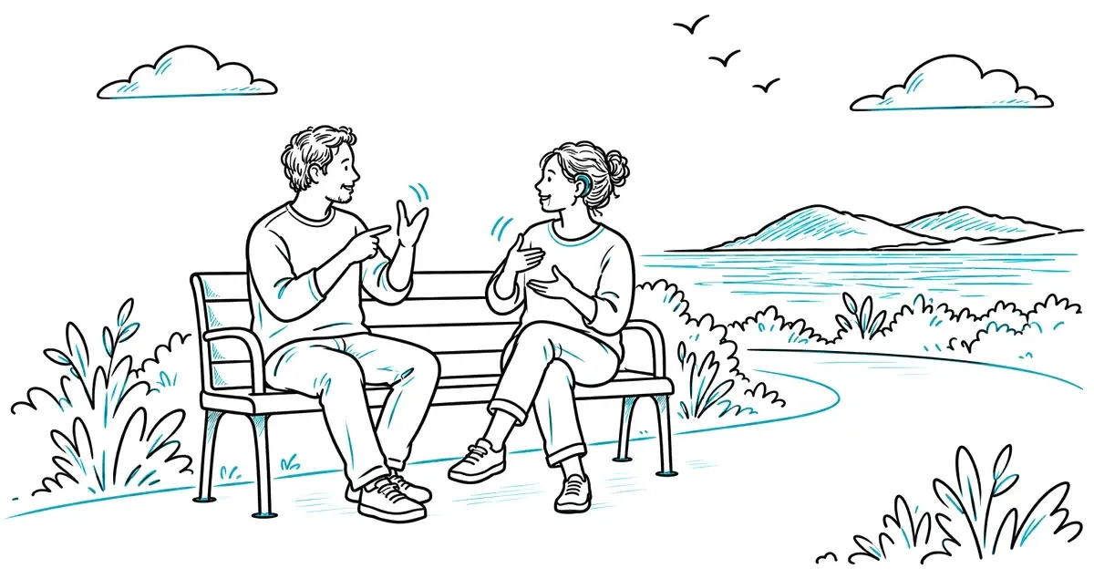 A support worker and a woman with a hearing aid chatting in sign language on a bench by the sea